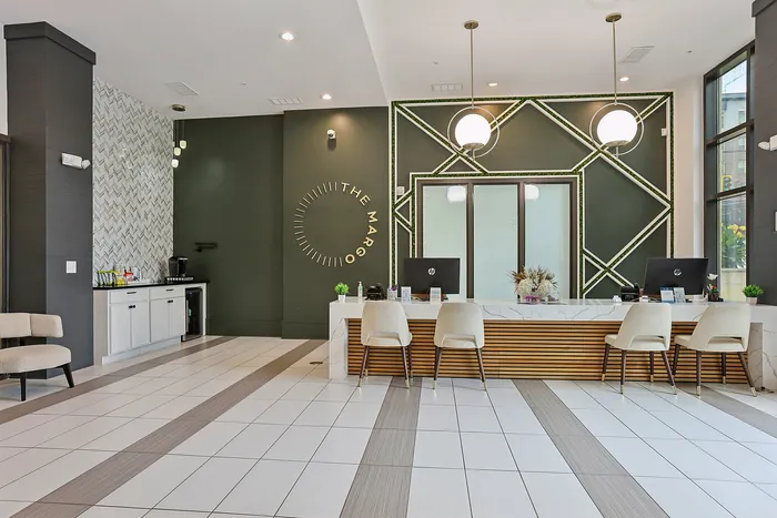 Modern apartment lobby with chic decor, featuring a welcoming reception desk, stylish lighting fixtures, and an elegant green accent wall displaying 'The Margo'.