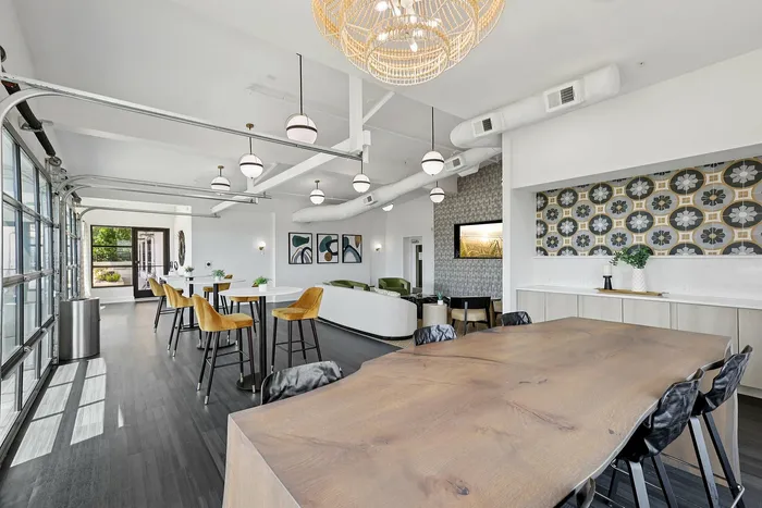Chic communal area with elegant wood dining table, stylish bar stools, modern decor, and large windows for natural light.