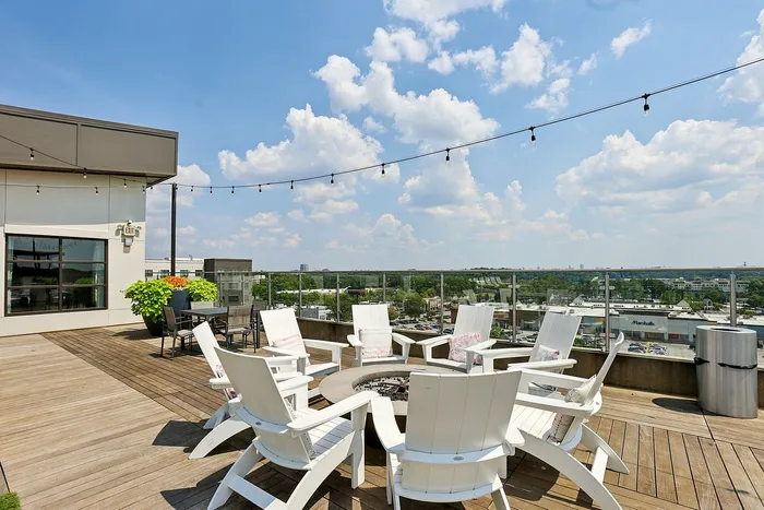 Inviting rooftop patio featuring stylish Adirondack chairs around a modern fire pit, with panoramic city views and ambient string lighting.