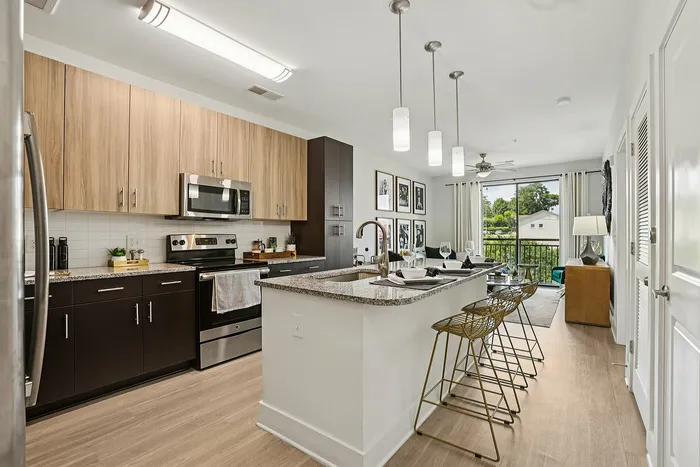 Modern open-concept kitchen with sleek countertops, stylish pendant lighting, and a cozy breakfast bar overlooking a sunlit living area with large windows.