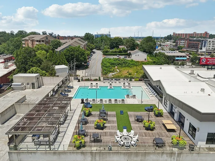 Luxurious rooftop view showcasing a sparkling pool, lush green spaces, and modern lounging areas under clear blue skies.