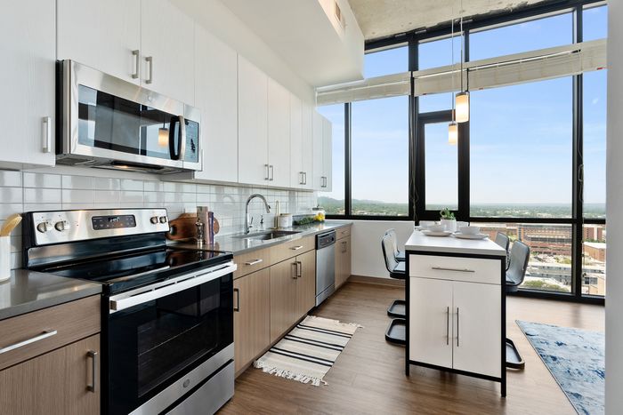 Modern kitchen with sleek stainless steel appliances, large windows offering panoramic city views, and a cozy dining area.