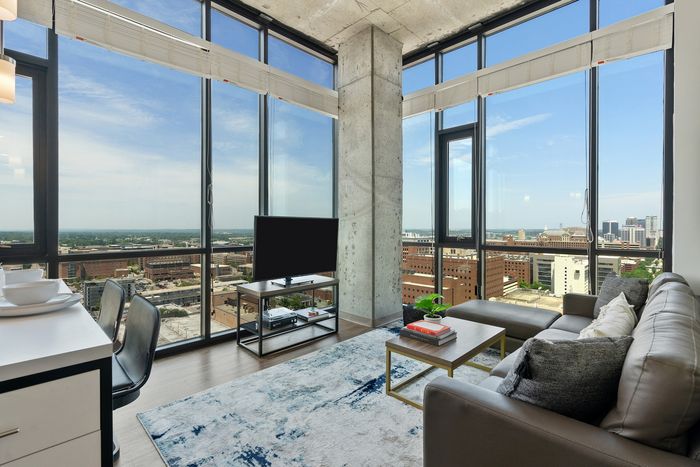 Sleek apartment living room with floor-to-ceiling windows offering stunning cityscape views, modern furnishings, and a cozy atmosphere.