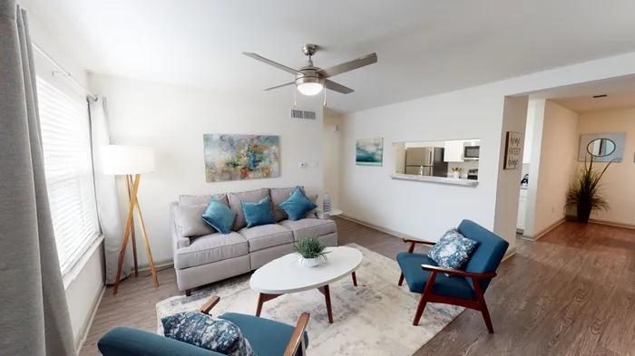 Inviting living room with modern decor featuring a cozy sofa, stylish blue armchairs, and a sleek ceiling fan, perfect for relaxation.