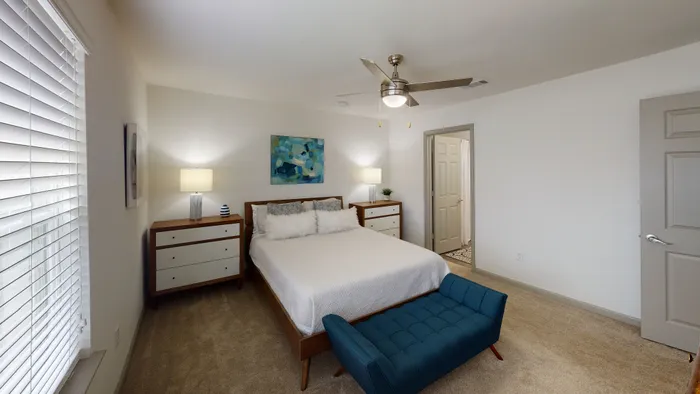 Inviting bedroom with modern decor, featuring a cozy bed, elegant side tables, and a chic blue bench, offering a serene retreat with soft lighting.