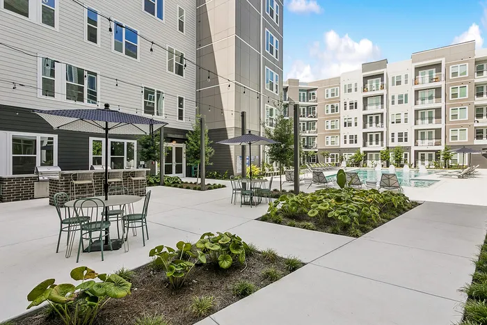 Chic urban courtyard featuring modern outdoor seating, lush greenery, and a sparkling pool surrounded by stylish apartment buildings.