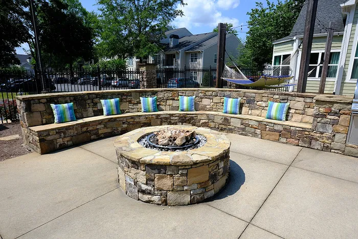 Charming outdoor patio with a stone fire pit surrounded by cozy seating and colorful cushions, ideal for relaxing under the open sky.