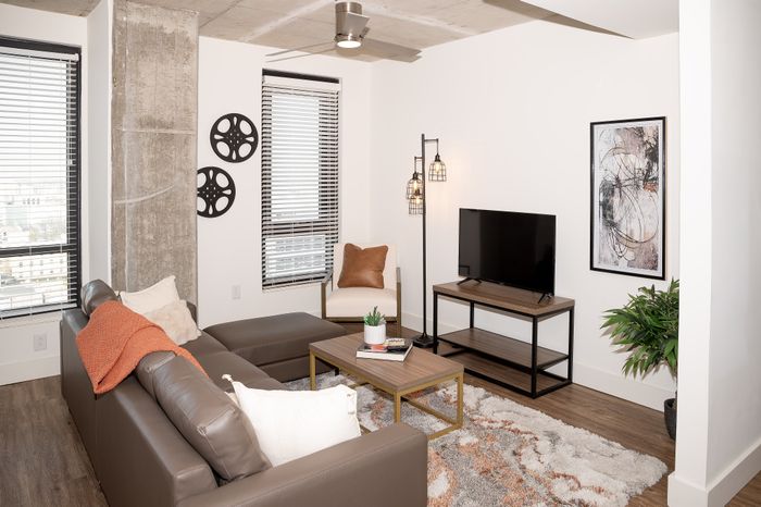 Modern living room with chic decor, featuring a cozy brown leather sectional, stylish floor lamp, and sleek flat-screen TV on a wooden stand.