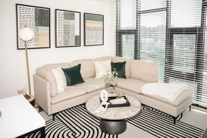 Bright and modern living room with a plush beige sectional, decorative cushions, and a stylish marble coffee table, highlighted by large windows and contemporary artwork.