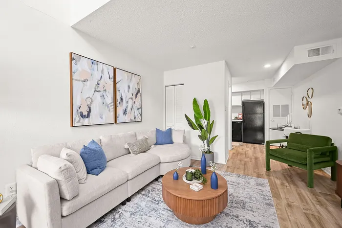 Contemporary living room with a cozy beige sectional, vibrant green chair, and abstract wall art; features a wooden coffee table decorated with modern vases and lush plant accents.