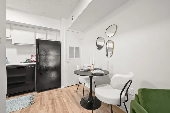 Chic apartment dining area with elegant black round table, plush white chairs, and modern mirrors enhancing the stylish space.