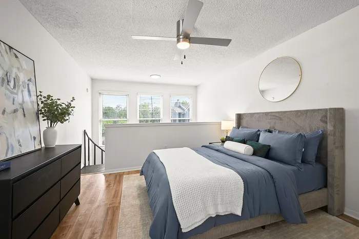 Bright and airy bedroom with elegant decor, featuring a stylish ceiling fan, plush bedding, and a sleek black dresser, perfect for a serene retreat.