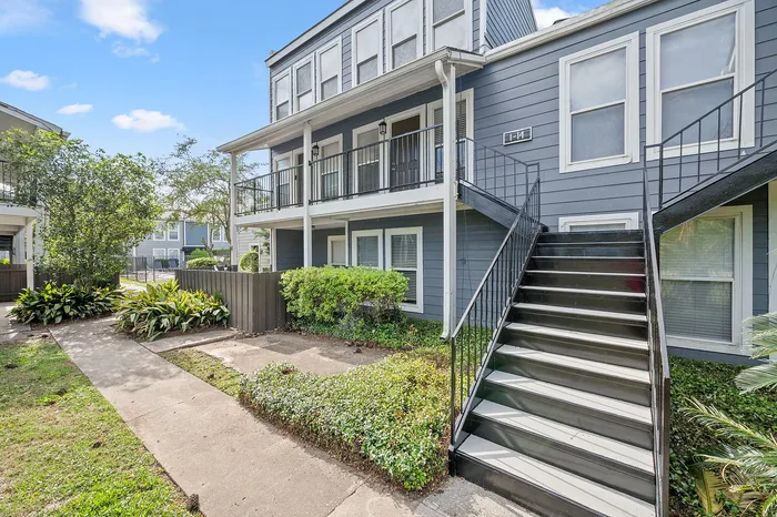 Charming apartment building with contemporary gray exterior, surrounded by lush greenery and a welcoming walkway.