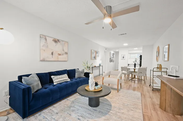 Bright and inviting living room with a plush blue sofa, chic decor, and an open dining area, featuring modern accents and a stylish floor lamp.