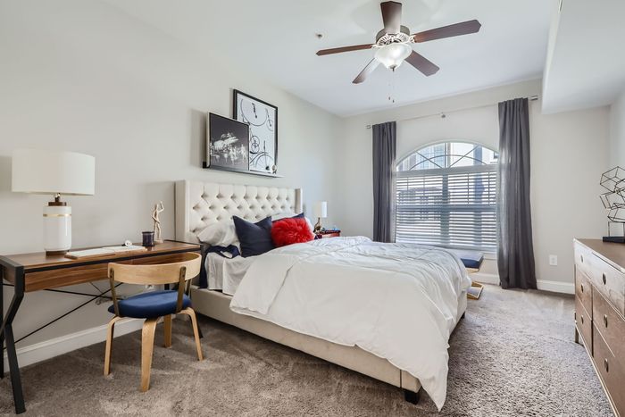 Elegant bedroom with plush carpeting, featuring a luxurious bed, stylish desk, and ample natural light from a large arched window.