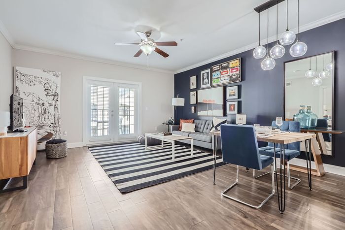 Bright and stylish living area with modern decor, featuring a cozy sofa, dining set, and unique lighting, complemented by a bold accent wall and natural light from large patio doors.