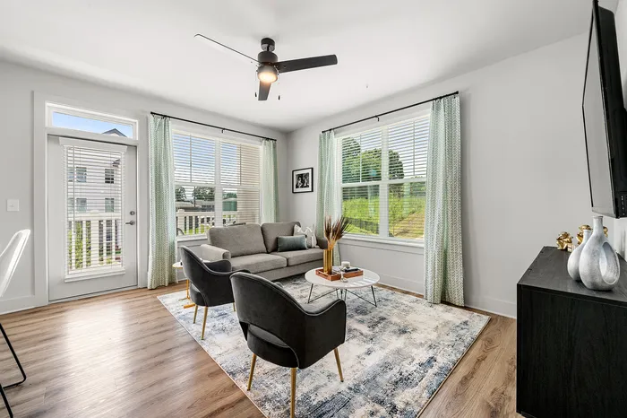 Bright and modern living room with large windows, stylish gray sofa, and chic armchairs, offering a serene view.