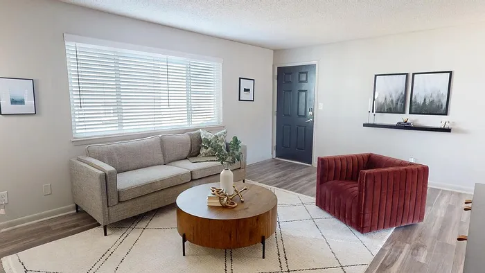 Inviting living room with modern decor, featuring a cozy gray sofa, stylish red armchair, and chic wooden coffee table on a light-patterned rug.