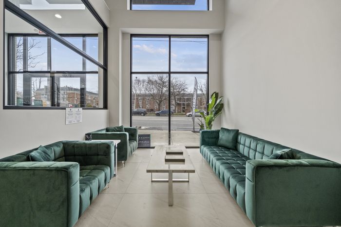 Elegant apartment lounge with plush green sofas and large windows offering a cityscape view.