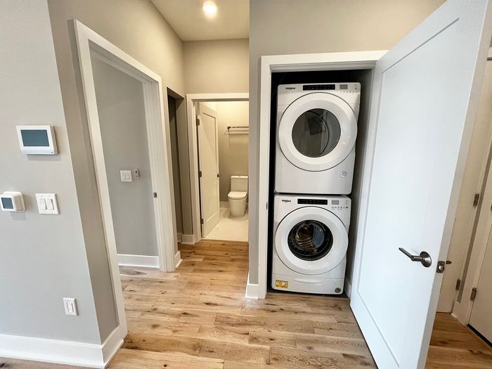 Modern apartment hallway featuring a stacked washer and dryer adjacent to a pristine bathroom.