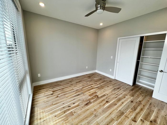 Sunlit bedroom with wooden flooring, built-in closet, and ceiling fan.