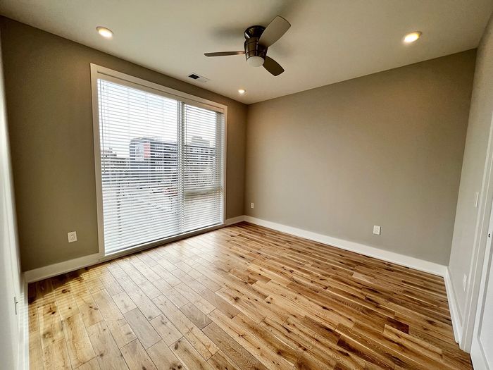 Inviting bedroom with wooden flooring, large window with blinds, and modern ceiling fan.
