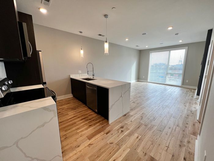 Bright open kitchen with a modern island and wooden floors leading to a sunlit living area.