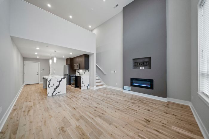 Sleek open-concept living area with modern kitchen, stylish island, elegant flooring, and a wall-mounted fireplace.