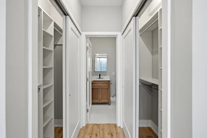 Elegant hallway with dual closets leading to a modern bathroom featuring a stylish vanity and wood accents.