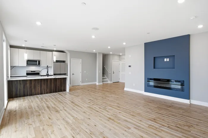 Modern open-concept living space featuring sleek hardwood floors, a stylish kitchen with stainless steel appliances, and a cozy blue accent wall.