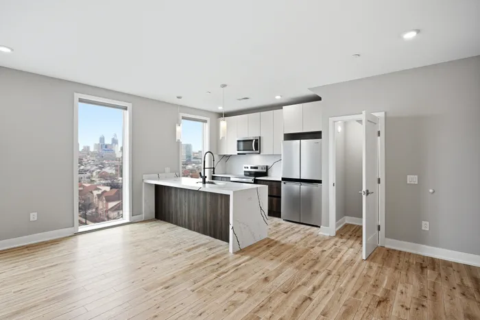Modern apartment kitchen with sleek appliances, island with marble countertop, and cityscape views through large windows.