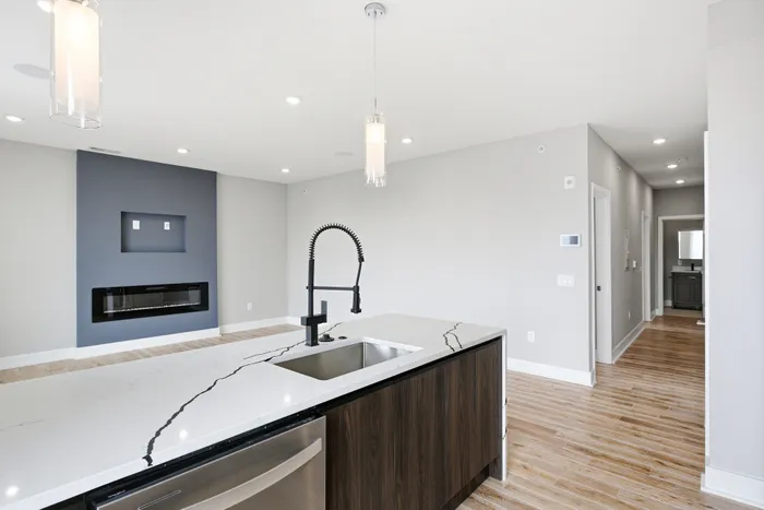 Modern apartment interior with sleek marble countertop, contemporary kitchen faucet, and elegant gray accent wall featuring a built-in fireplace.