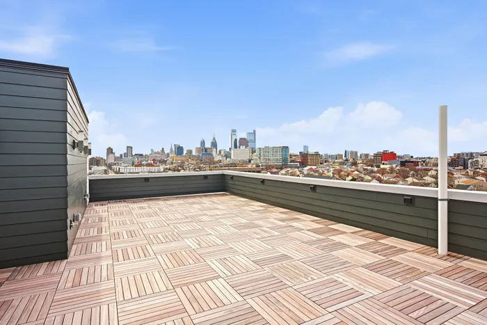 Expansive rooftop terrace with modern deck flooring offering stunning city skyline views under a clear blue sky.