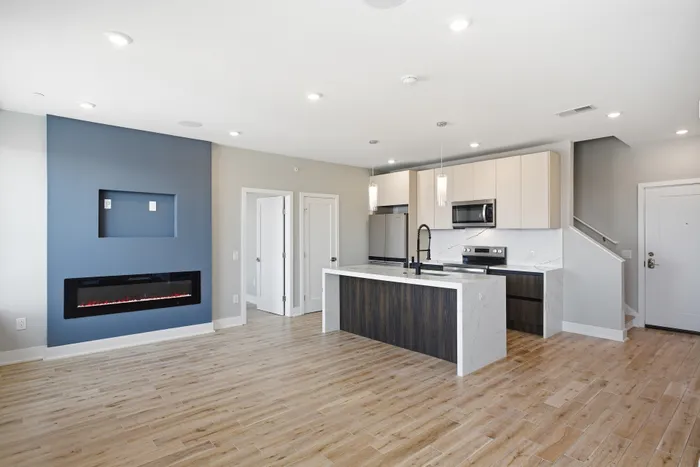 Modern open-concept apartment showcasing sleek kitchen with island, elegant fireplace, and bright living area on hardwood floors.
