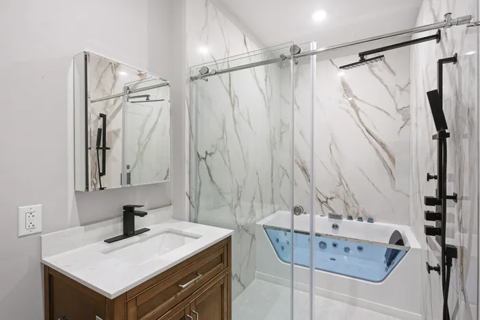 Luxurious bathroom featuring elegant marble walls, modern vanity, and a sleek glass shower with a hydrotherapy tub.