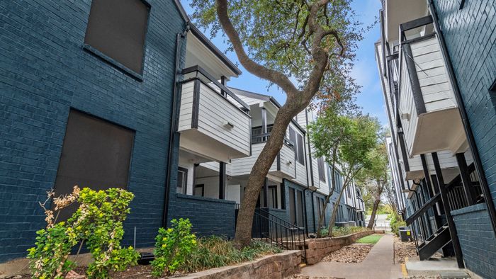 Charming apartment exterior with modern balconies, lush landscaping, and a welcoming pathway.