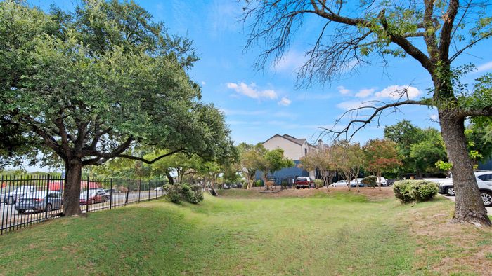 Charming apartment complex surrounded by lush green trees and vibrant landscaping under a clear blue sky.