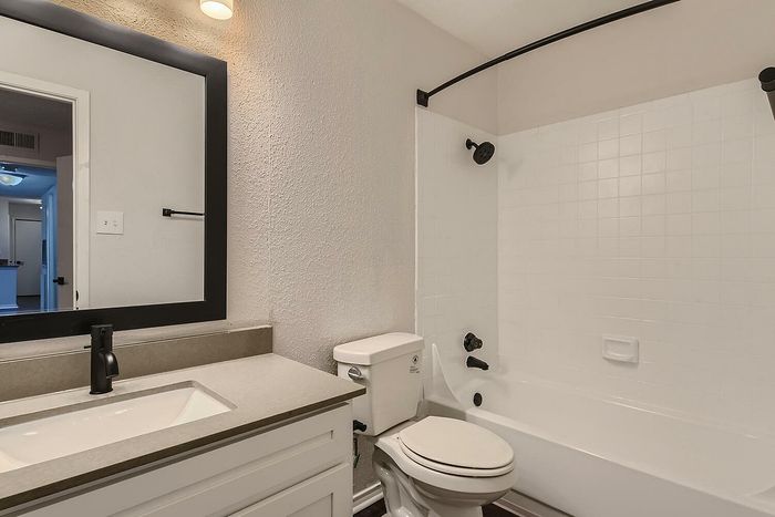 Modern bathroom featuring sleek fixtures, a large mirror, and a pristine bathtub with elegant tile detailing.