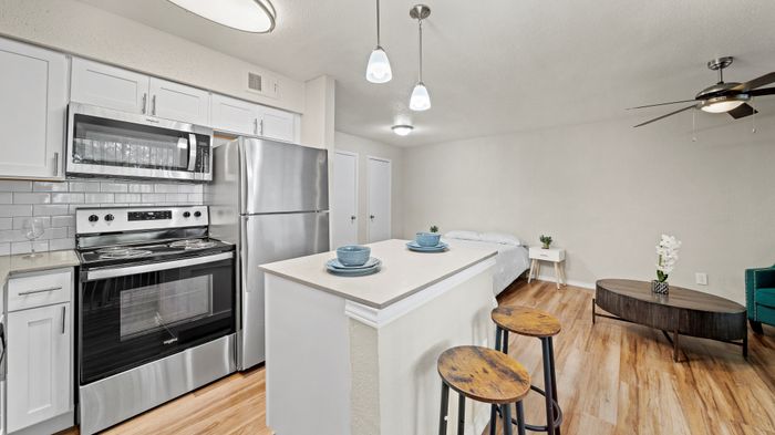 Modern open-plan kitchen and living area with stainless steel appliances, elegant island seating, and cozy sleeping nook, featuring sleek lighting and warm wood flooring.