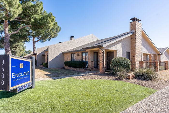 Charming Enclave Apartment Homes with modern exterior, lush green lawn, and inviting entrance under clear blue skies.