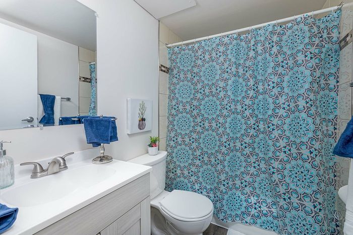 Bright and inviting bathroom with elegant blue floral shower curtain, modern sink and fixtures, and tasteful decor for a refreshing ambiance.