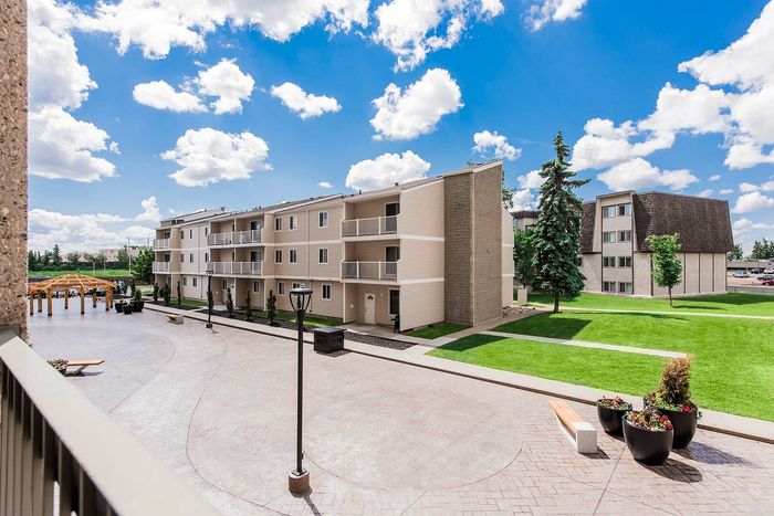 Charming apartment complex with modern facade, spacious balconies, and beautifully landscaped courtyard under a bright blue sky.