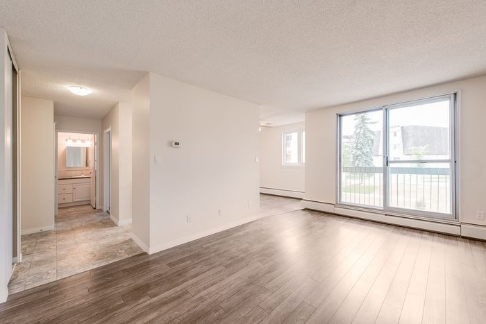 Bright and inviting apartment living area featuring sleek wooden floors, large sliding glass doors, and a glimpse into a modern bathroom.