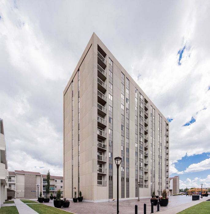 Modern high-rise apartment building under a bright sky, featuring sleek architecture and well-maintained surroundings.