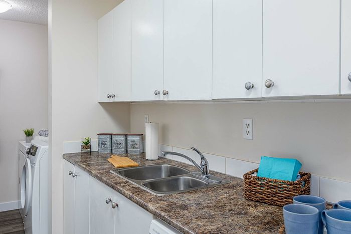 Contemporary kitchen with stylish white cabinets, a dual-basin sink, and sleek countertops, leading to a convenient in-home laundry area.