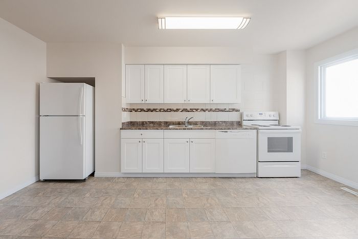 Bright and modern kitchen with sleek white cabinets, a spacious countertop, and shiny appliances including a refrigerator and stove.