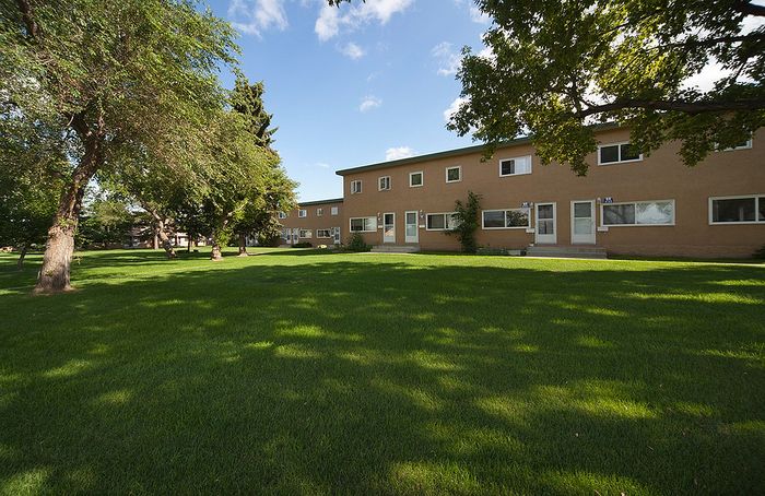 Charming townhouse with lush green lawn, surrounded by mature trees and a serene atmosphere.
