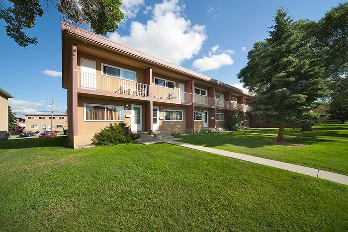 Charming apartment building with spacious balconies, nestled in lush green surroundings under a clear blue sky.