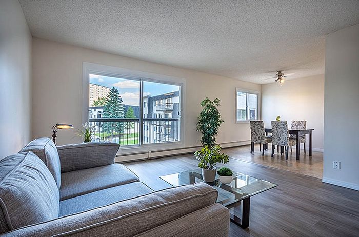 Bright and inviting living room with large windows showcasing a scenic view, featuring modern furniture and an elegant dining area.