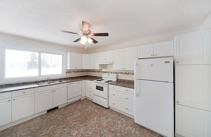 Bright and spacious kitchen with modern white cabinetry, large window, and sleek tile flooring.
